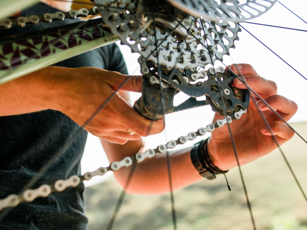 Two hands, seen through the spokes of a bike wheel, adjust a derailleur. 