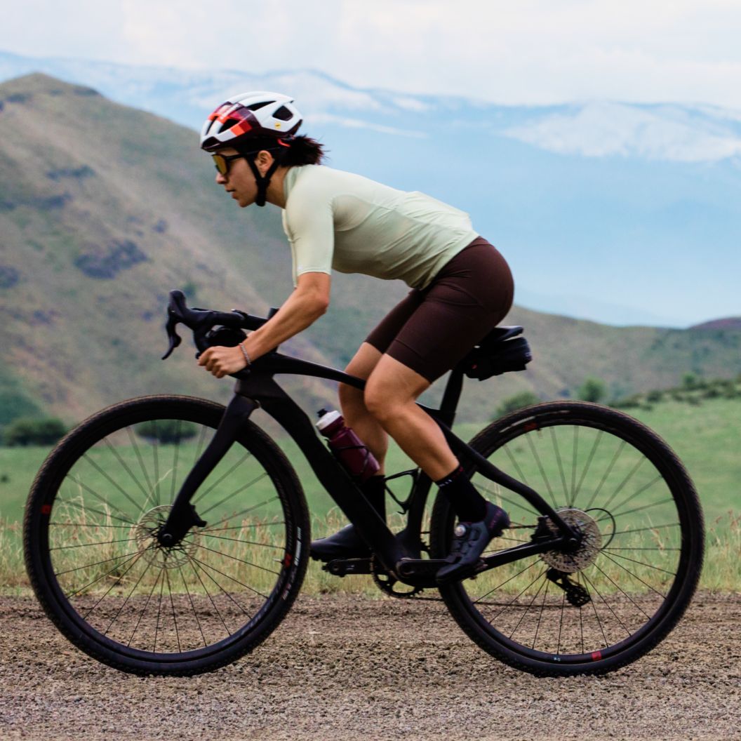 A rider on a Pinarello Grevil pedals a flat groad with snow-capped mountains in the background.