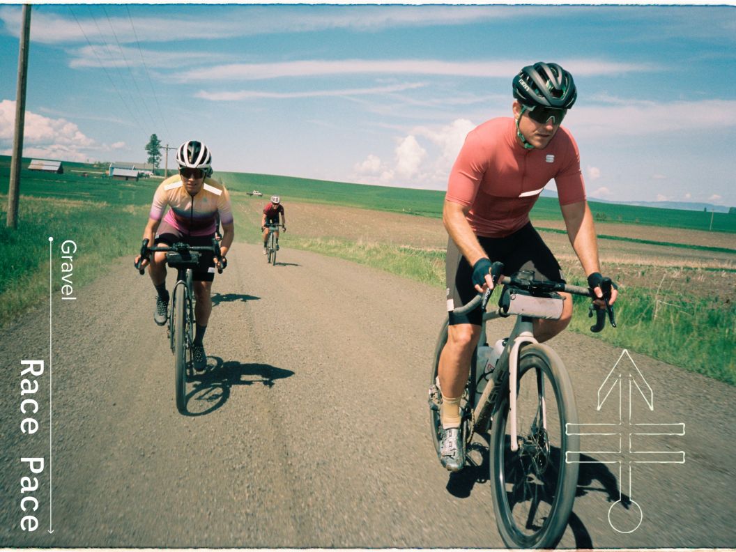 Three gravel riders enjoy a fast ride next to grassy farmland on a sunny day.