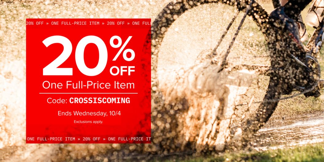 A red block with text reading “20% off one full-price item with code CROSSISCOMING, ends Wednesday, 10/4, exclusions apply” is shown over a photo of a rider’s wheel going through a mud puddle.