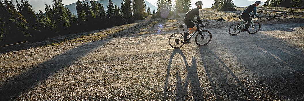 Two cyclists ride on gravel at sunset