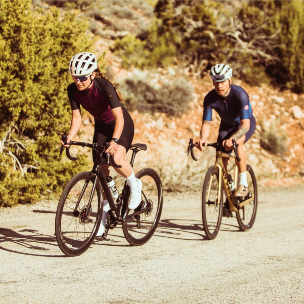 Two riders pedal up a climb in summer.