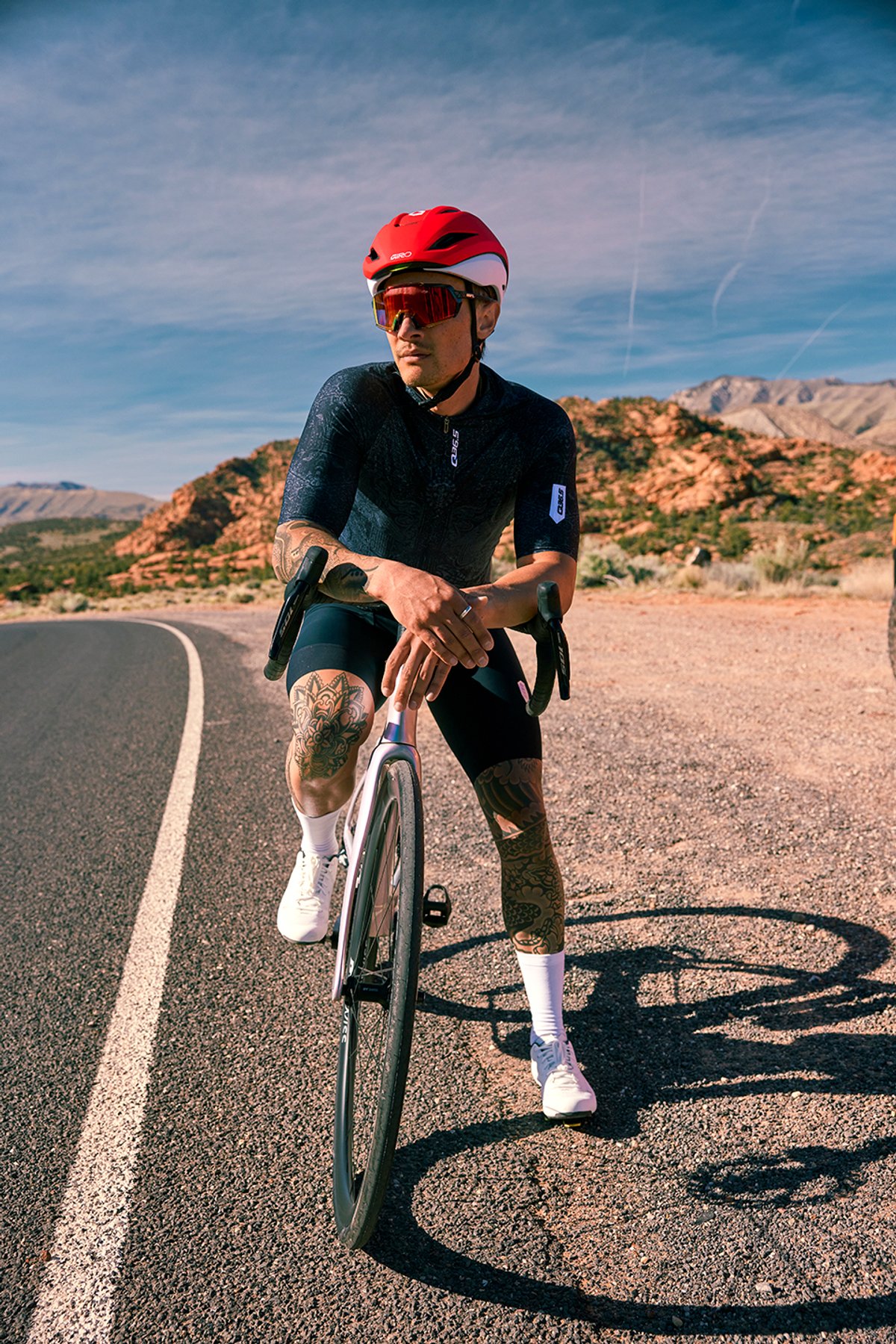 Road cyclist wearing cycling bib shorts and road cycling shoes riding Pinarello road bike on paved road through arid terrain