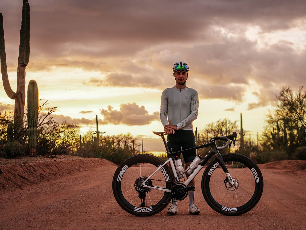 Gravel rider stadning with their bike on dirt road in the desert.
