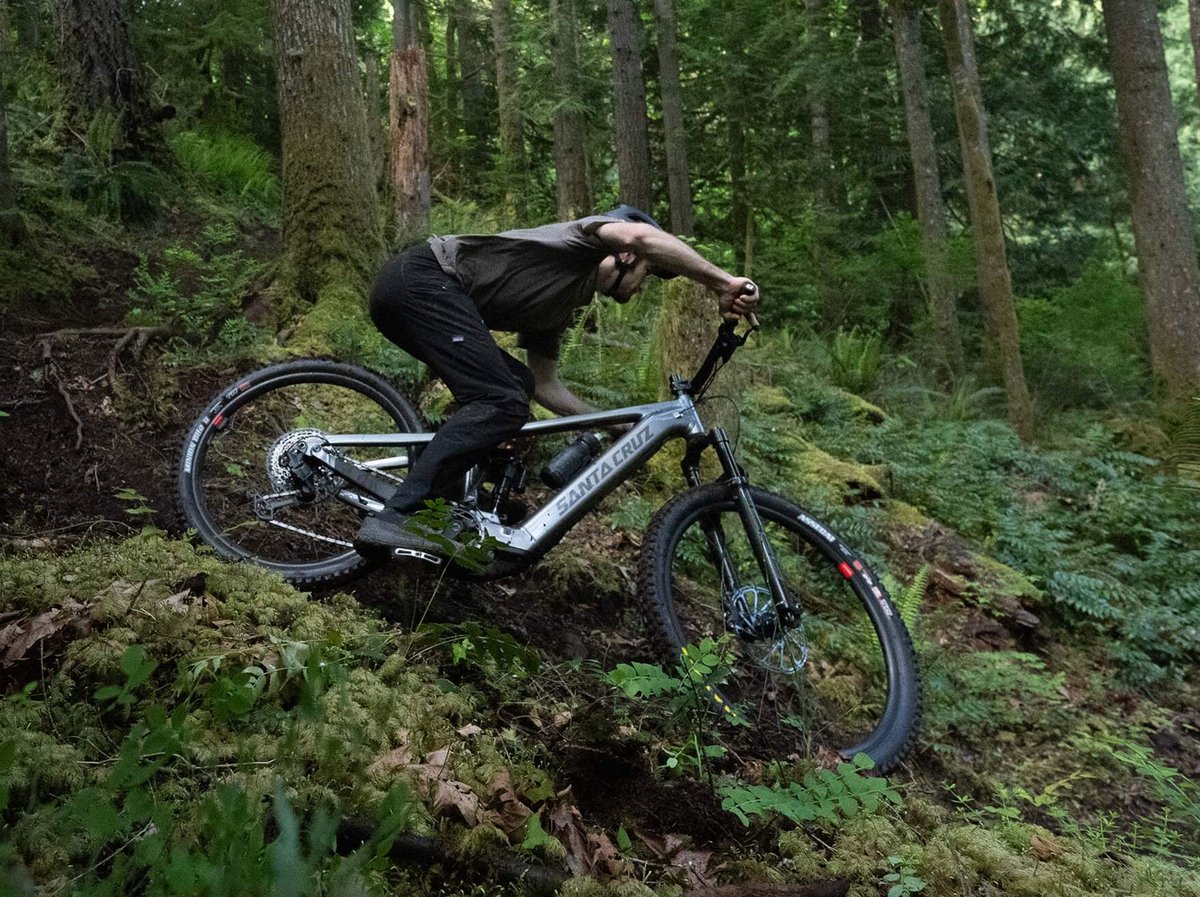 Rider descending a technical forested trail on a Santa Cruz Vala AL electric mountain bike.