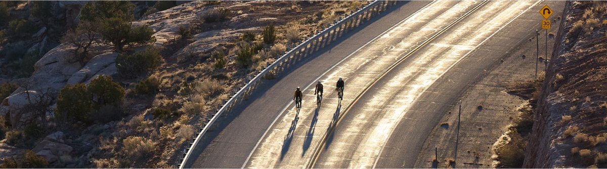 Three riders push the pace on a curved road during golden hour.