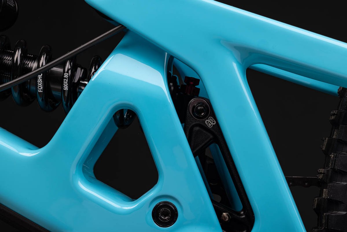 Close-up of full-suspension enduro mountain bike rear linkage and flip chip adjustment hardware on teal carbon frame