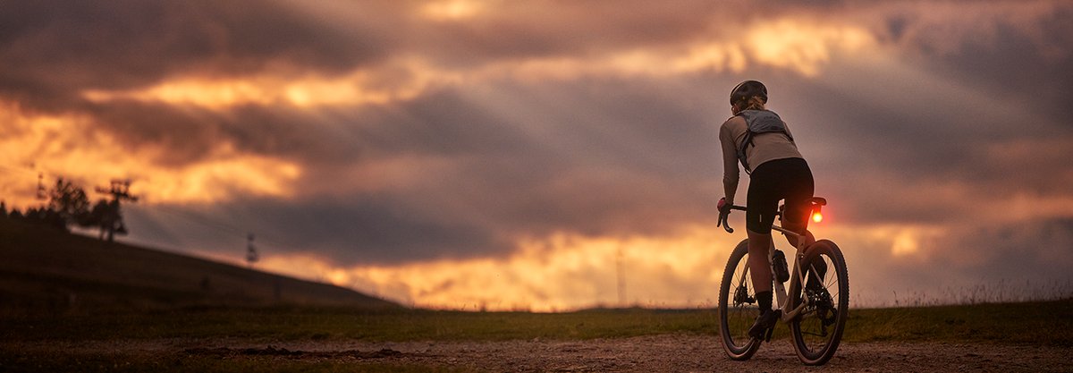 Gravel cyclist riding into sunset with bike light illuminated
