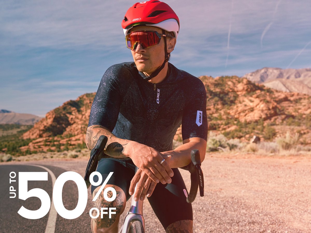 Cyclist resting on a road bike against a sun-baked desert highway backdrop. Memorial Day Sale — up to 50% off.