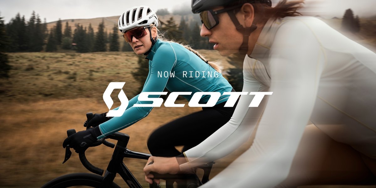 Two cyclists blur past the landscape. Text overlay reads: Now Riding Scott.