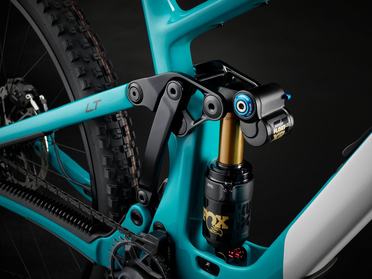 Detail of the Sixfinity suspension linkage on a teal and white frame, connecting to a Fox Float X2 Factory shock with gold-anodized shaft.