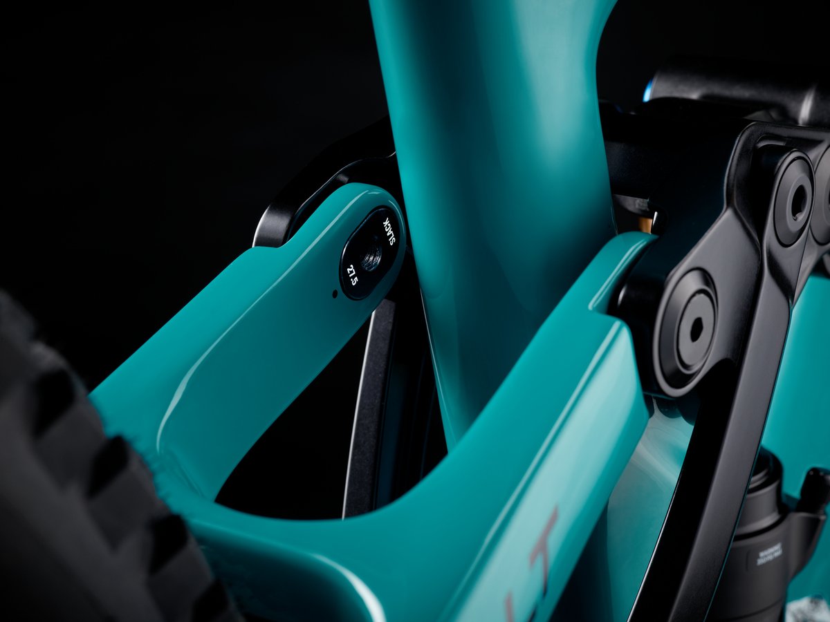 Close-up of a teal frame's flip chip insert, labeled "SLACK" with "21.5" markings, set into the chainstay/seatstay junction near the rear shock.