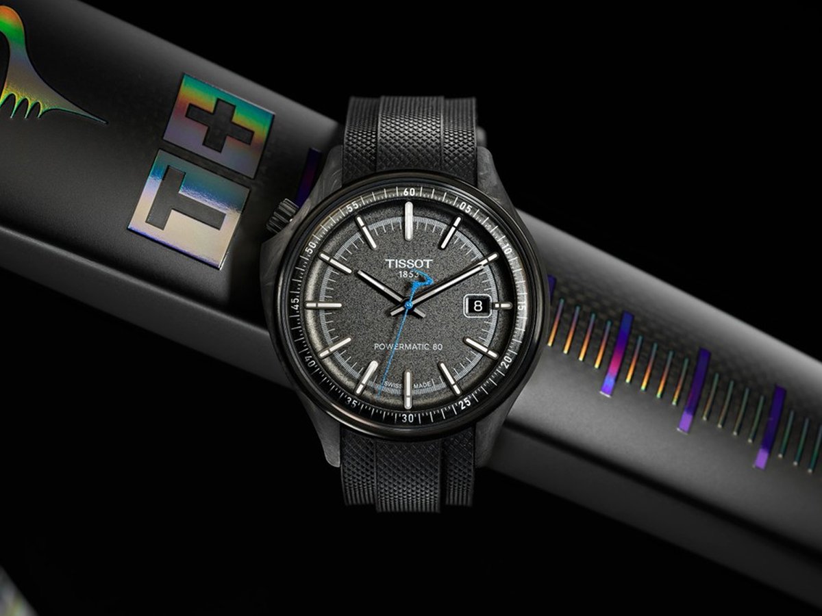 Tissot Powermatic 80 watch in black, resting on the iridescent carbon tube of the Pinarello Dogma F Edizione Speciale against a dark studio background.