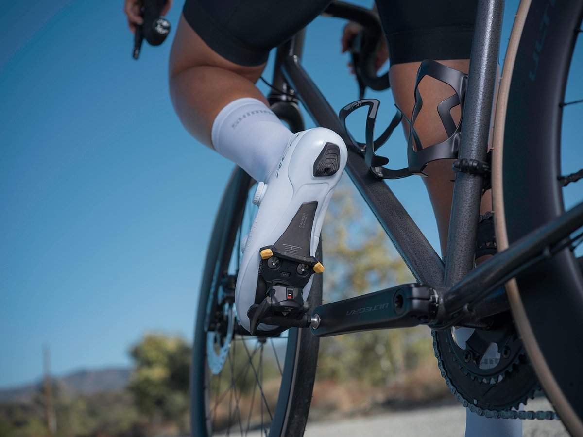 Cyclist's foot in a white RC810 shoe clipped into an Ultegra pedal, low angle showing the sole and cleat against the crank