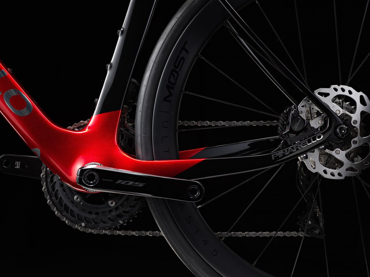 Pinarello red carbon road bike with Shimano 105 drivetrain, cassette, and disc brakes on deep section wheels against dark studio background