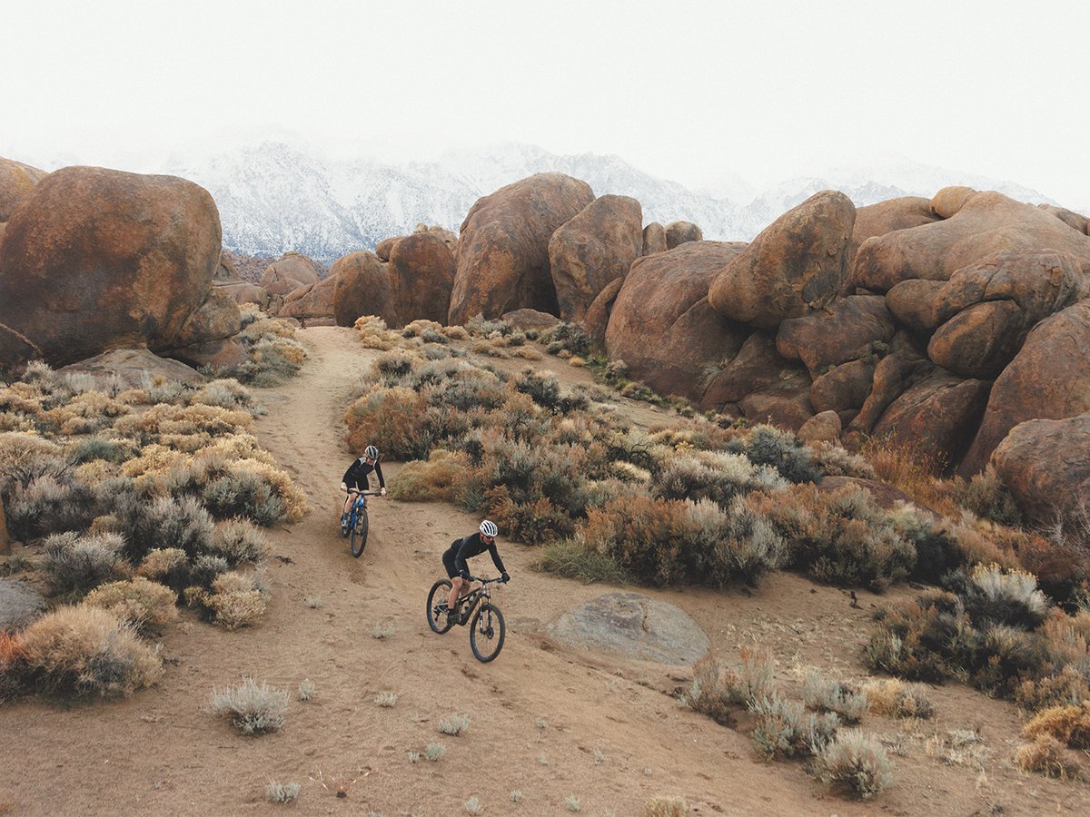 Two riders descending in rocky desert terrain.