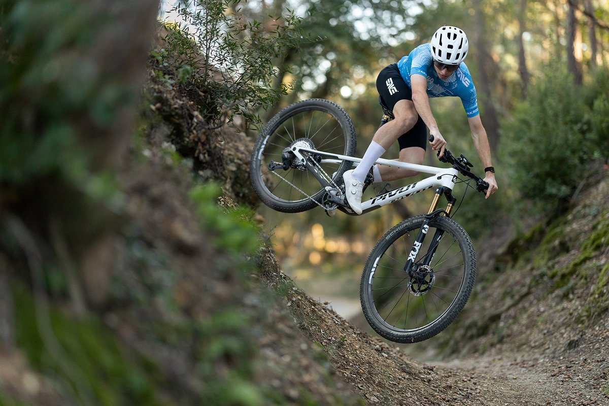 Rider cornering the Pivot Mach 4 SL carbon XC mountain bike on forest singletrack.