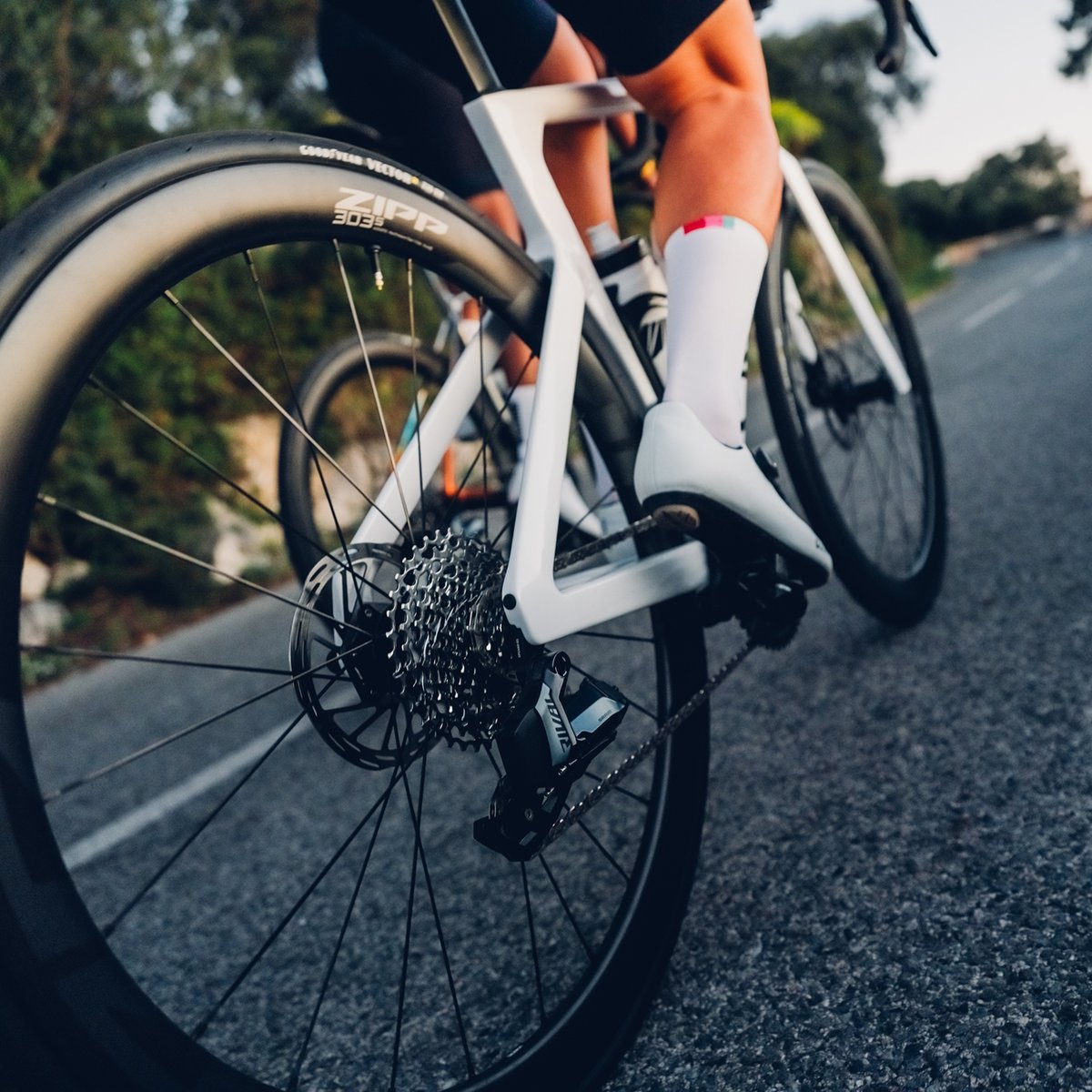 A white road bike equipped with top-of-the-line SRAM components. It’s rider is also equipped with pristine white socks and shoes.