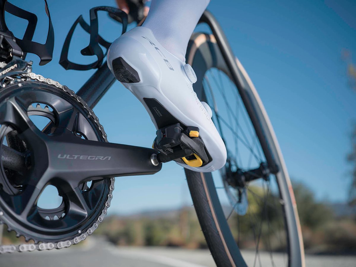 Cyclist's shoe clipped into an Ultegra pedal, close crop on crank and wheel, bottle cage visible, blue sky background