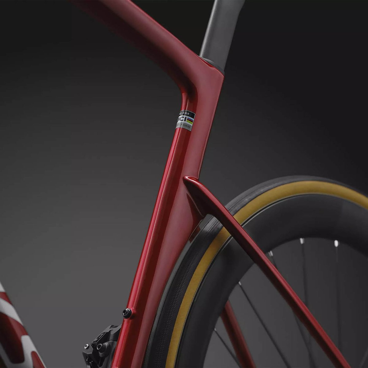Detail of the red Tarmac SL9 front triangle showing the down tube-to-head tube junction, UCI approval sticker, and tan-sidewall tire on a deep-section carbon wheel.