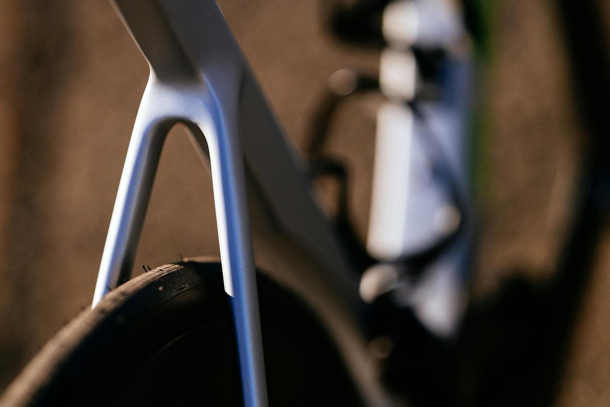 Close-up of carbon road bike fork leg and tire clearance detail showing aero fork blade profile against warm neutral background