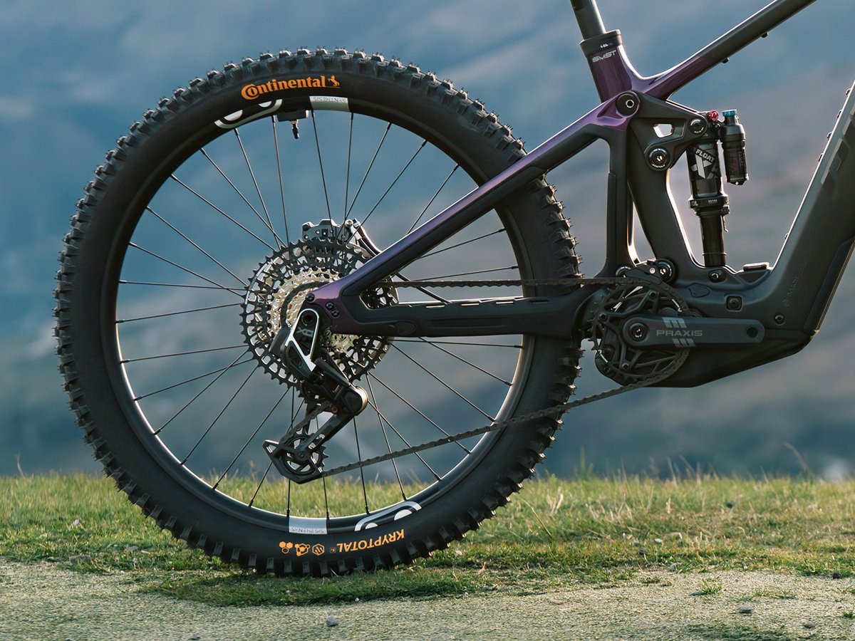A close-up side view of the rear half of a purple and black full-suspension mountain bike, fearuting the wheel, drivetrain, and shock.