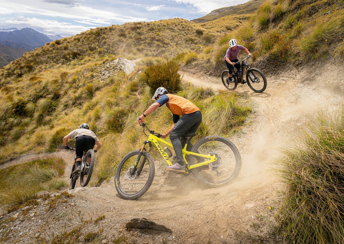 three people ride mountain bikes down a trail