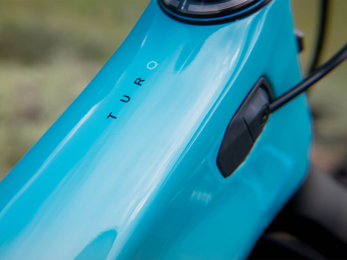 Close-up of the glossy turquoise downtube on the Yeti MT, showing the TURQ carbon logo and internal cable port.