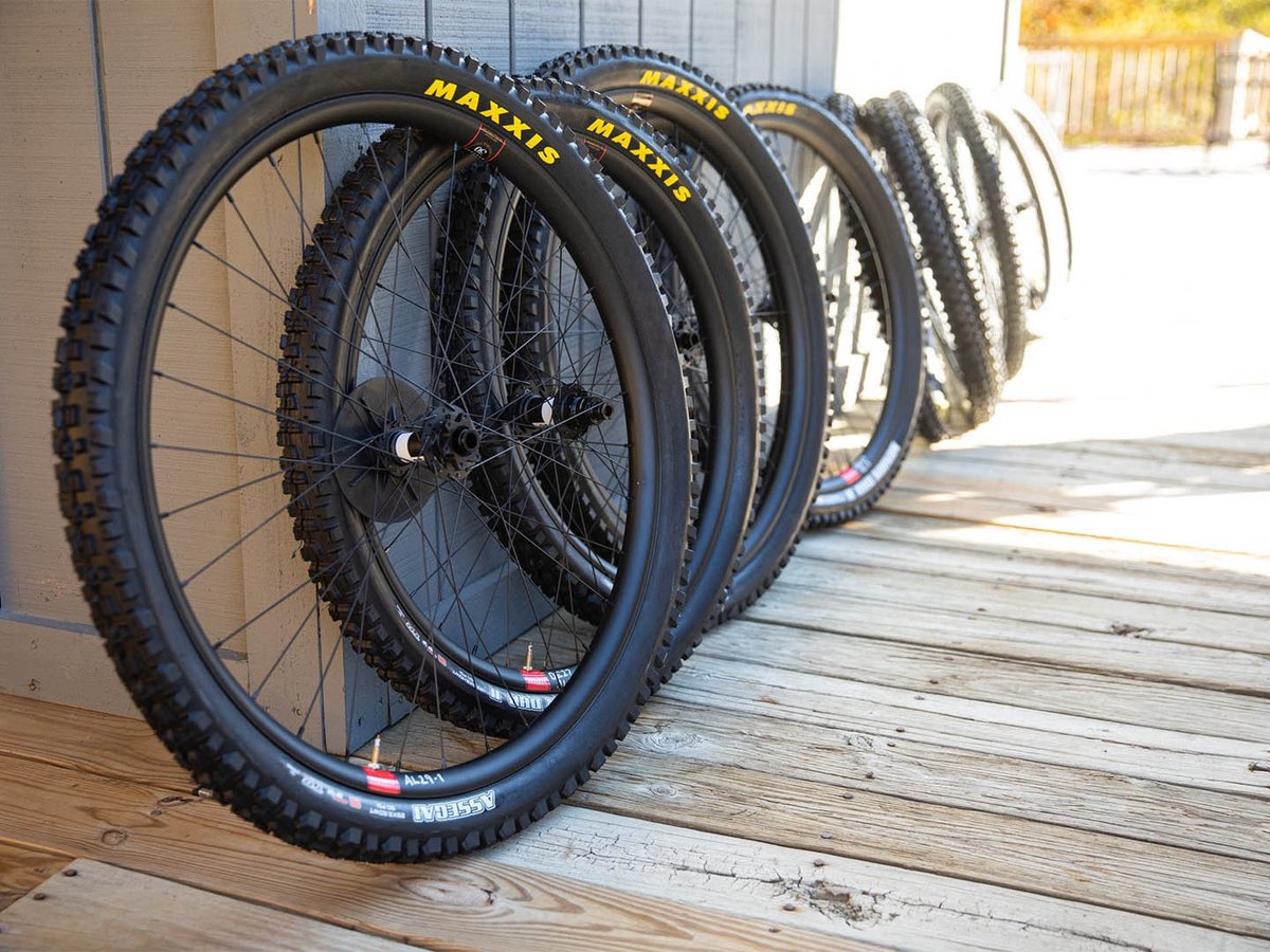 Four Reserve mountain bike wheelsets with Maxxis tires leaned against a building on a wood deck, receding in a row.