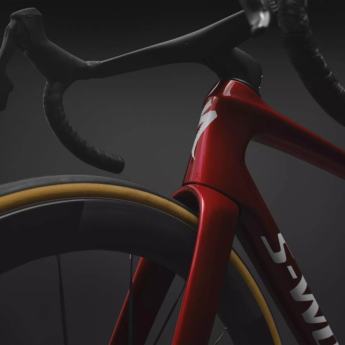 Close-up of the red Tarmac SL9 head tube and top tube junction showing the Specialized S logo, with drop bar and tan-sidewall deep-section wheel visible.