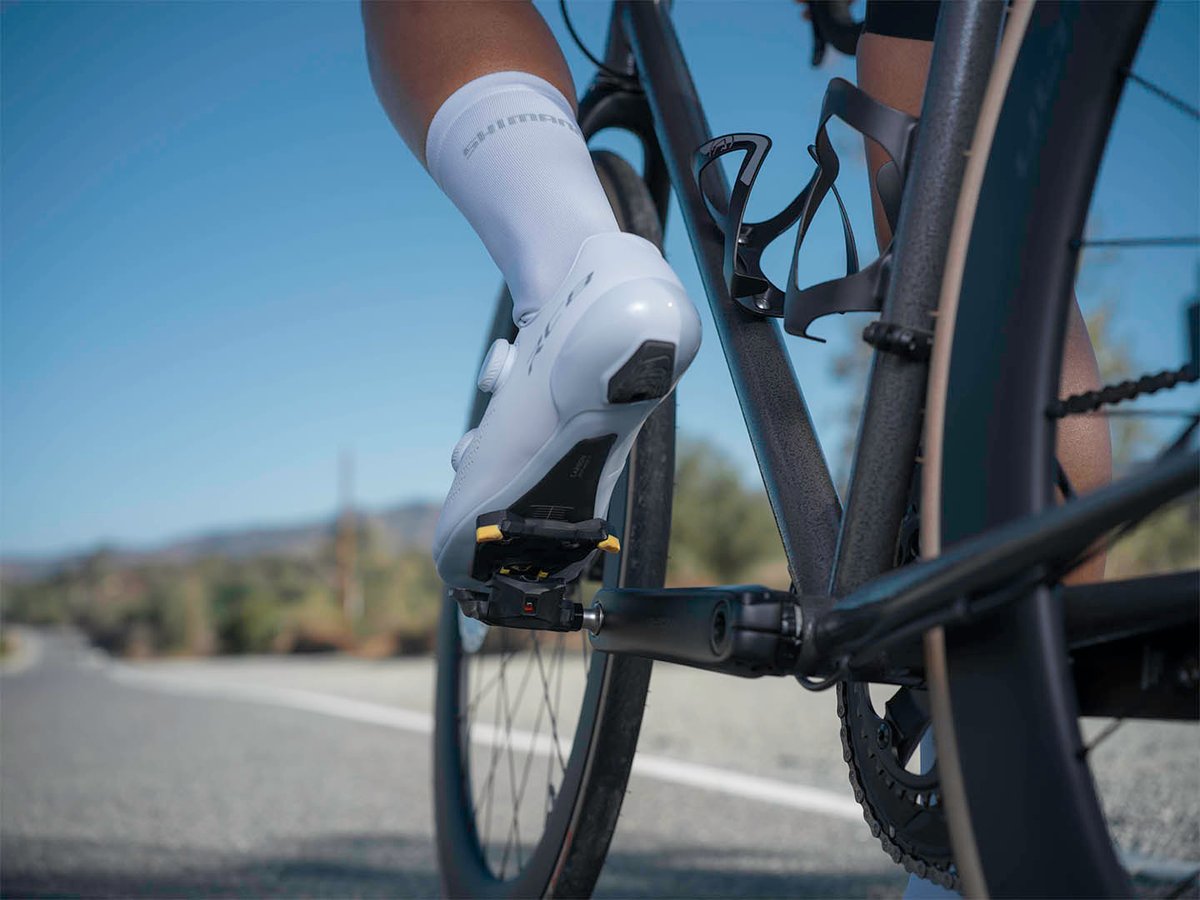 Cyclist's white shoe approaching a pedal mid-motion, close crop, road visible below