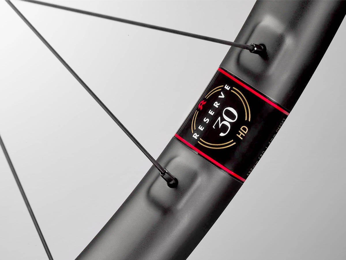 Close-up of a Reserve 30 HD carbon mountain bike rim showing the label with  "30 HD" branding, with crossed spokes visible behind.