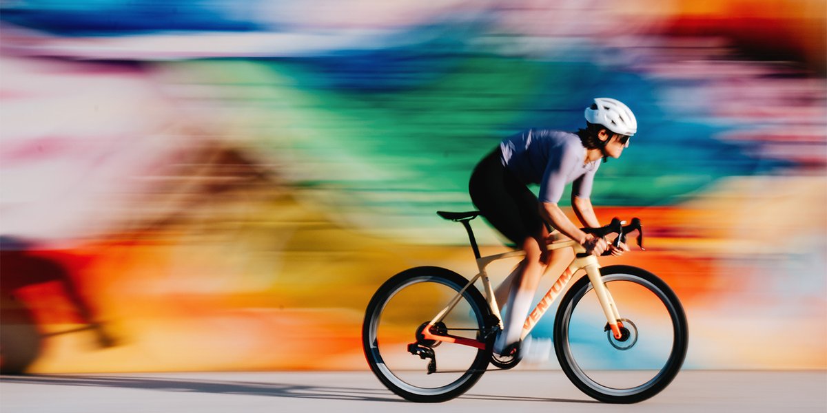 Road cyclist riding fast in blurred image in fornt of colorfully painted wall.