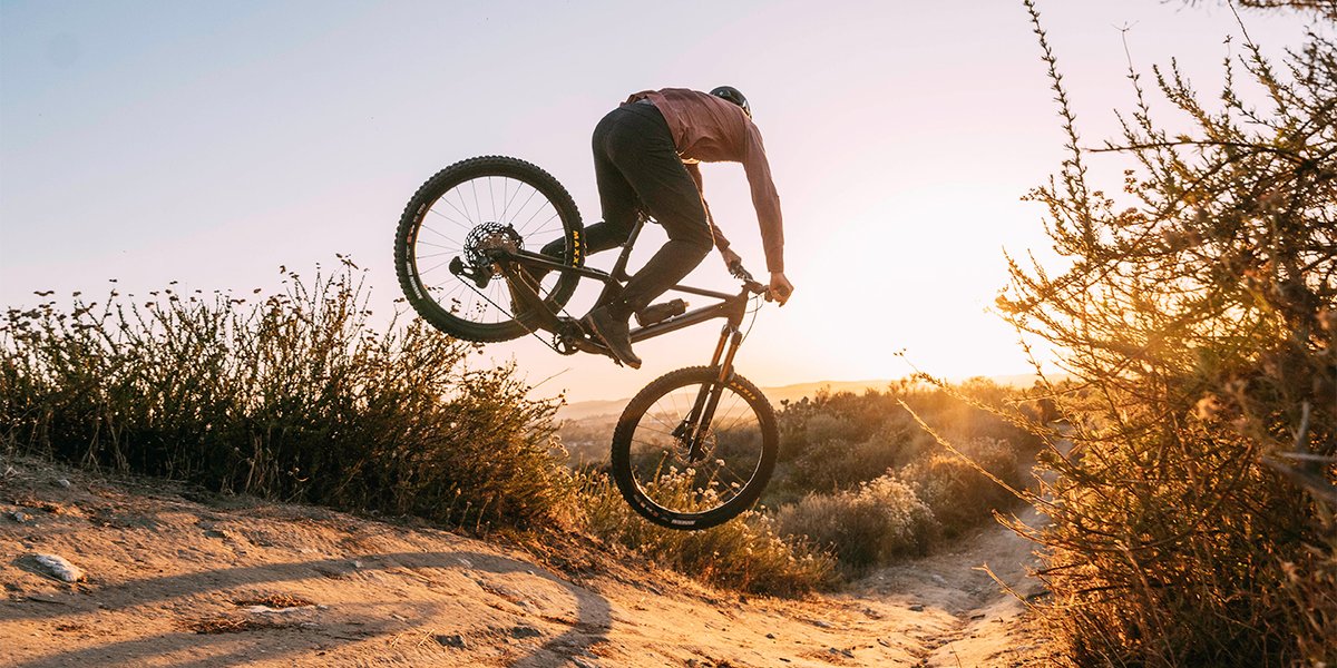 Claude responded: A mountain biker pulls a wheelie on a dirt trail at golden hour, with scrubby desert vegetation and hills visible in the background.A mountain biker pulls a wheelie on a dirt trail at golden hour, with scrubby desert vegetation and hills visible in the background.