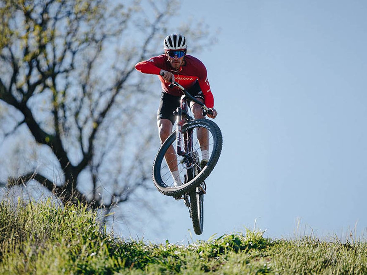 XC cyclist getting air on lip of grassy hill.