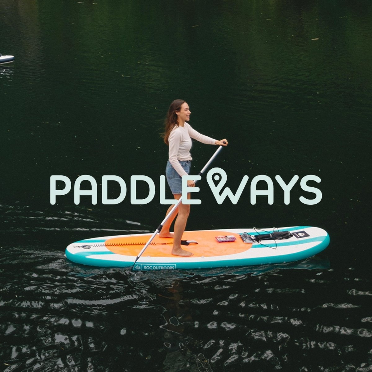 A smiling paddler stands on a teal-and-orange inflatable SUP on dark, calm water, paddle in hand. Featuring the Paddleways logo overlaid.