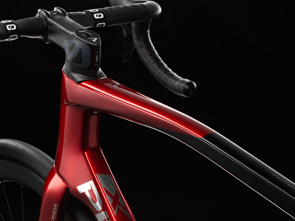 Pinarello red carbon road bike headtube and top tube detail with MOST stem and drop handlebars against dark studio background