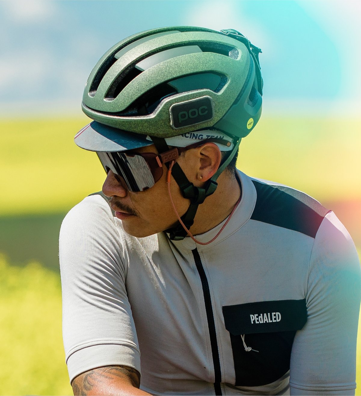 A cyclist wearing a green POC helmet and a light gray cycling jersey.