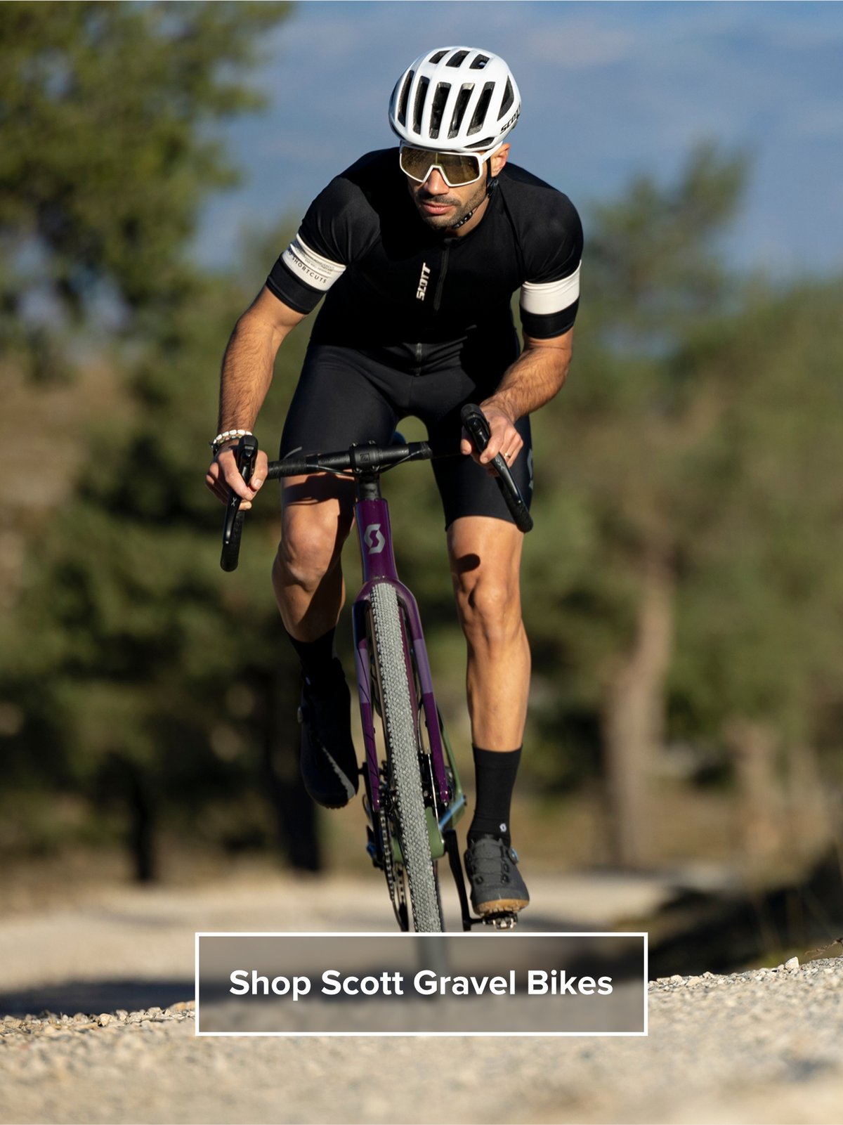 A cyclist powers up a gravel road. Text overlay reads: Shop Scott Gravel Bikes