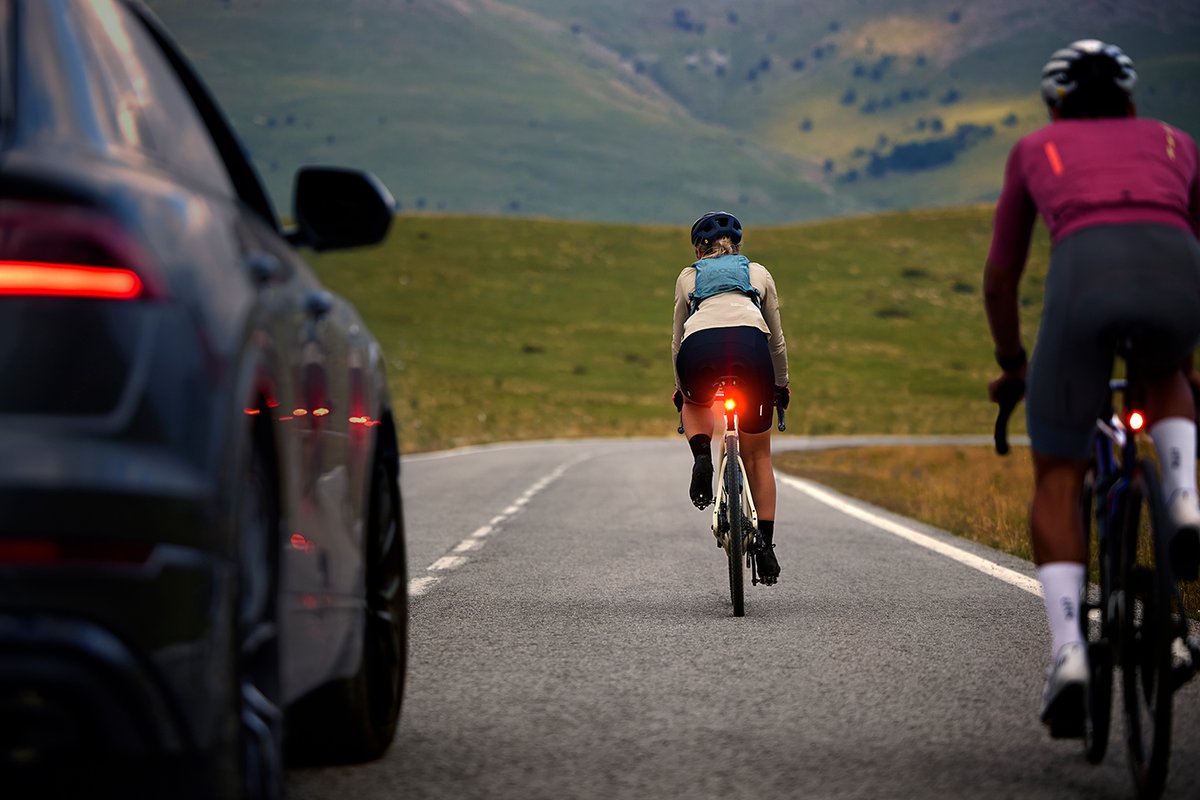 Road cyclists with illuminated rear lights riding near vehicle traffic