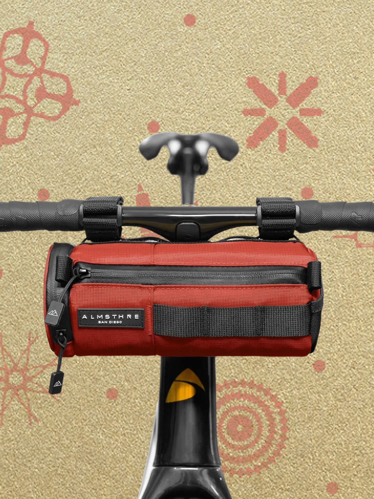 A red handlebar bag labeled "Almsthre" attached to the handlebars of a bicycle, with a bike themed wrapping paper background.