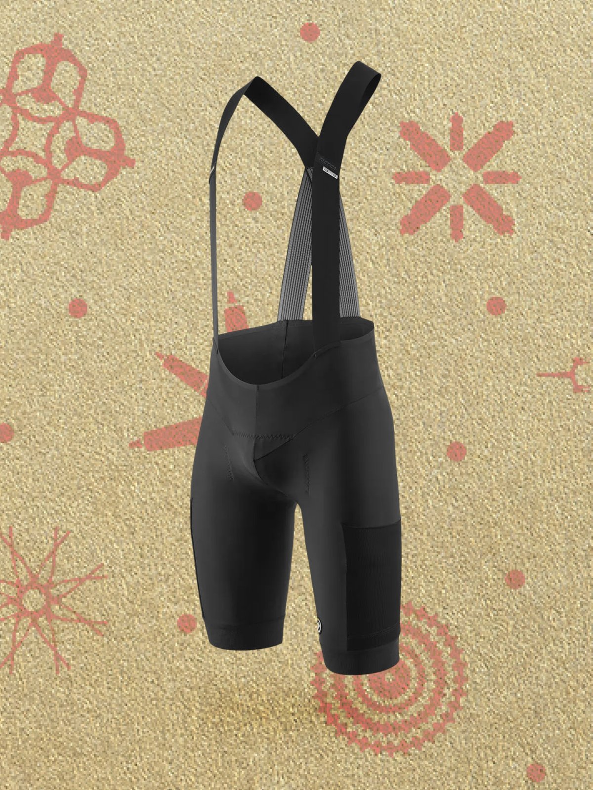 A pair of black cycling bib shorts with shoulder straps shown against a gold background decorated with red holiday patterns and red stripes.