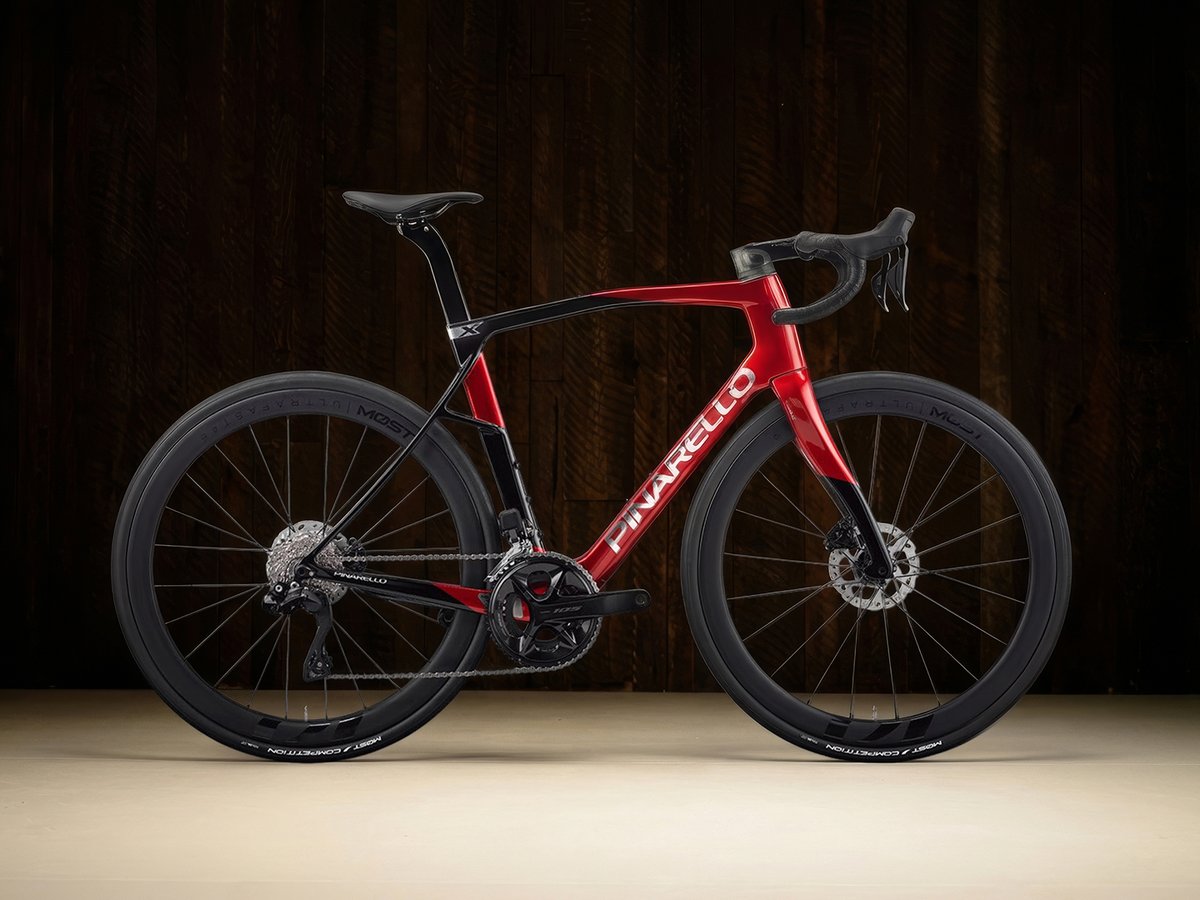 The Pinarello X5 road bike in a bold red-to-black gradient, shown in a side profile against a dark wood background.