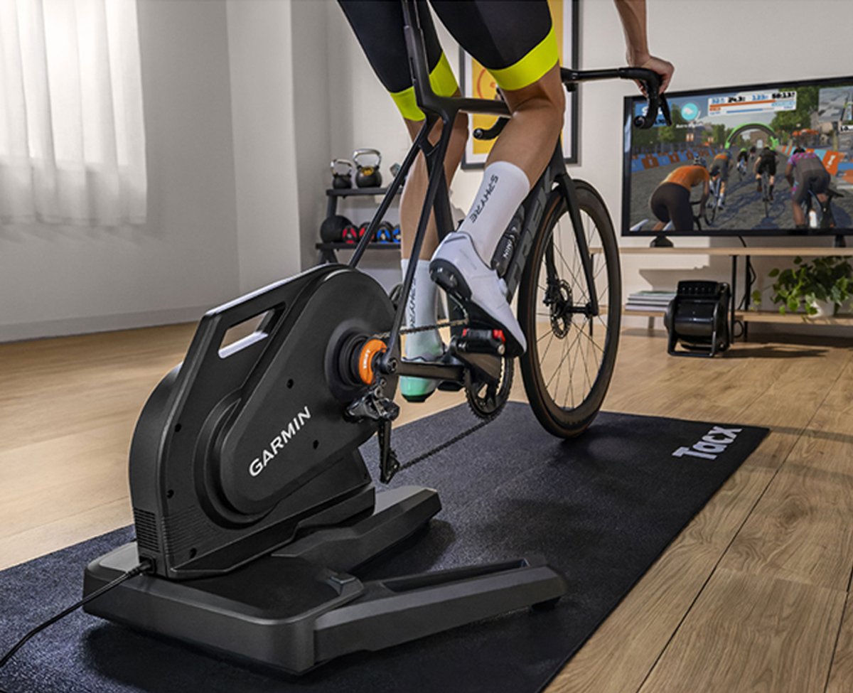 A person rides their bike on the Garmin Tacx Nera Trainer, watching a race simulation on their TV.