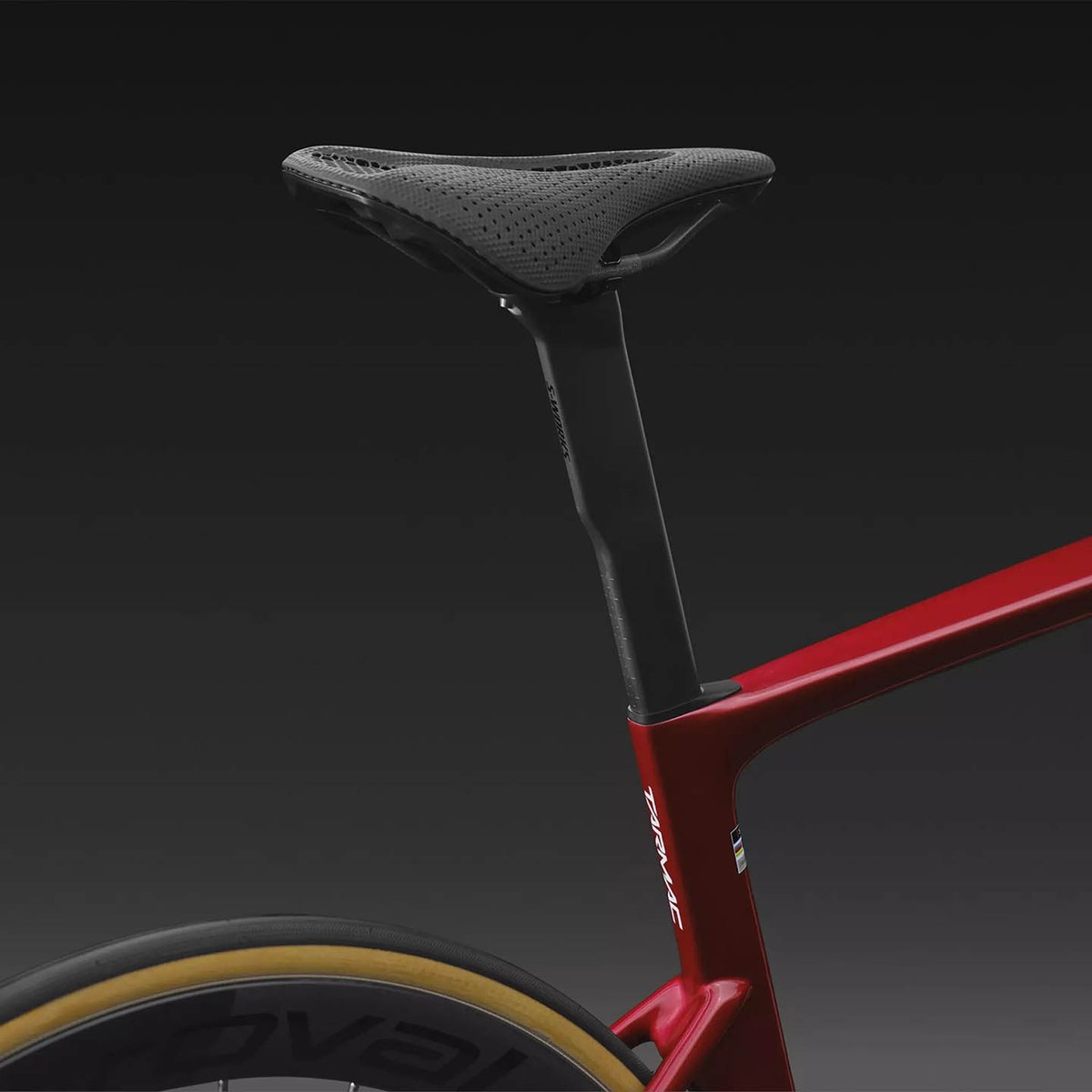 Black perforated Specialized saddle on a carbon seatpost mounted to the red Tarmac SL9 seat tube, with Roval deep-section wheel and tan sidewall tire below.