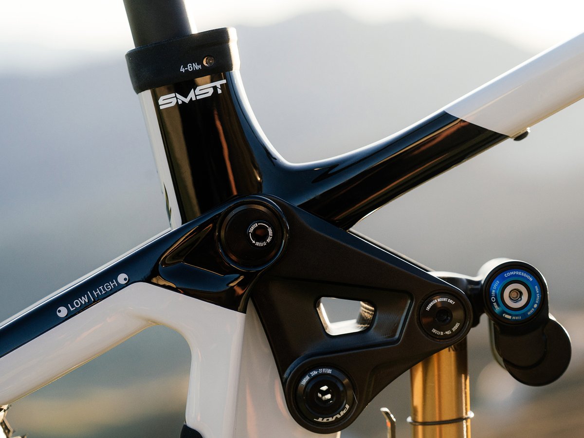 A close-up of a white and black full-suspension mountain bike frame shows the upper linkage, pivots, and seat tube.