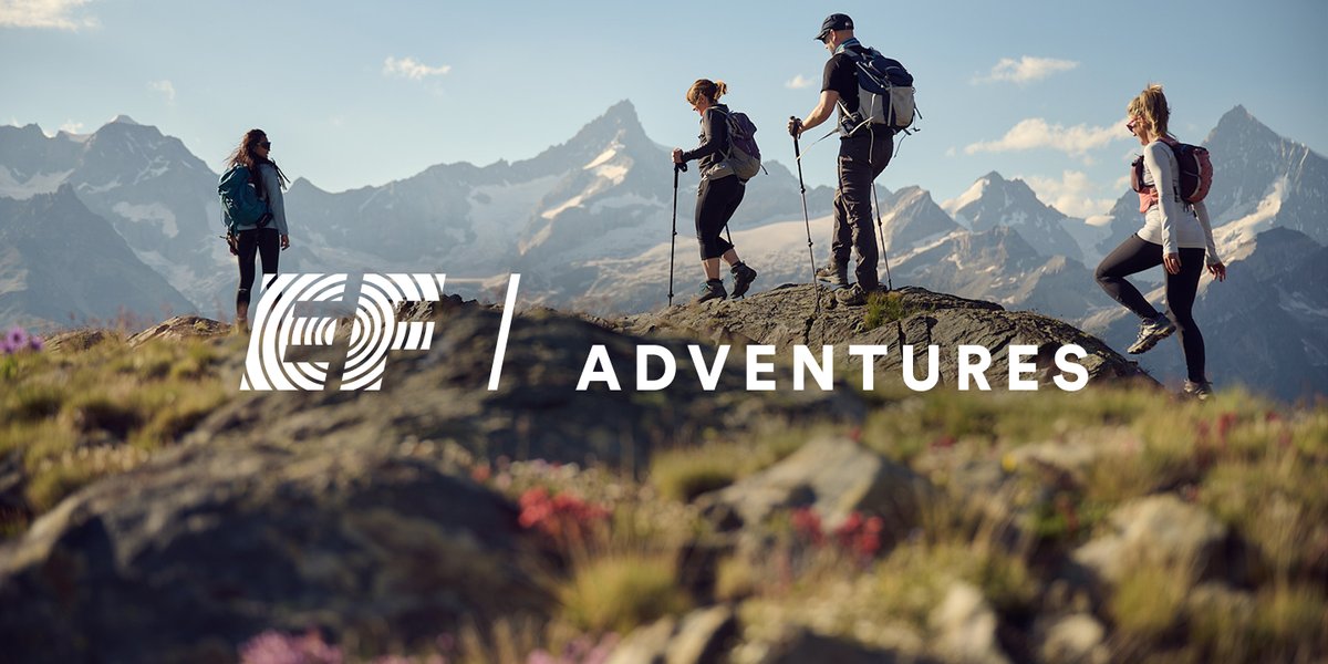 Group of hikers on a granite ridge overlooking an alpine mountain range, featuring the EF Adventures logo.