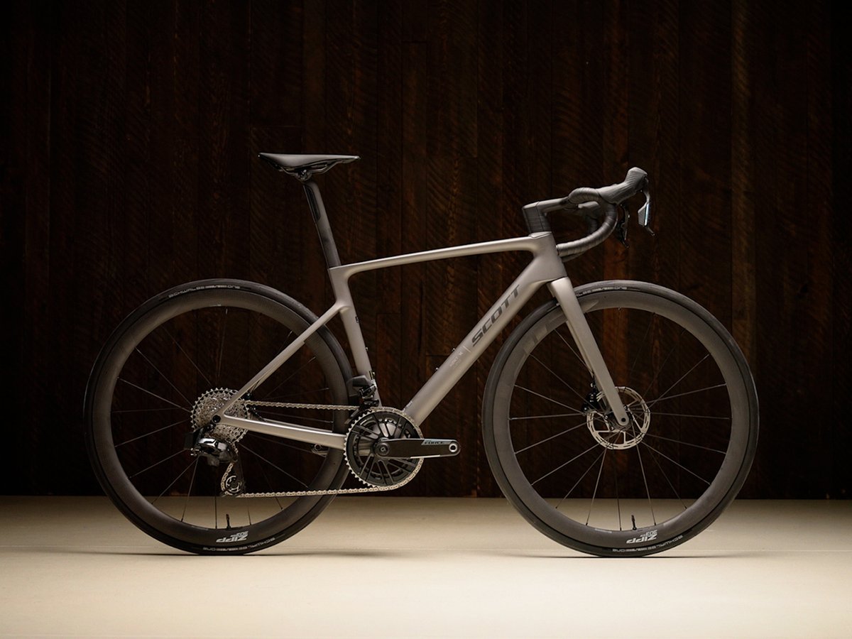 The Scott Addict RC road bike in matte silver-grey, shown in a side profile against a dark wood background.