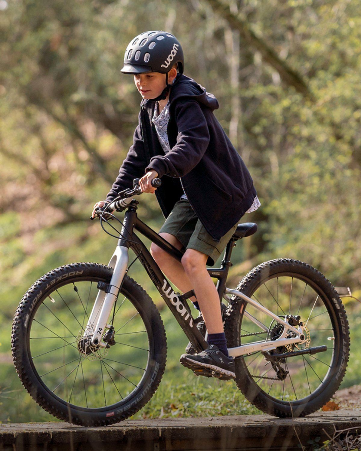 kid wearing helmet biking over a wooden boardwalk feature.