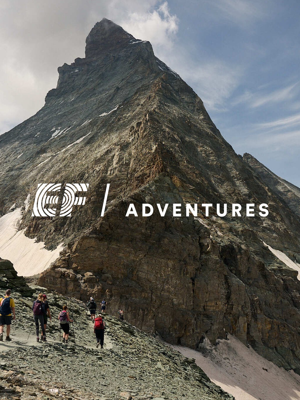 Group of hikers ascending a rocky alpine scree field beneath a dramatic  mountain peak, featuring the EF Adventures logo.